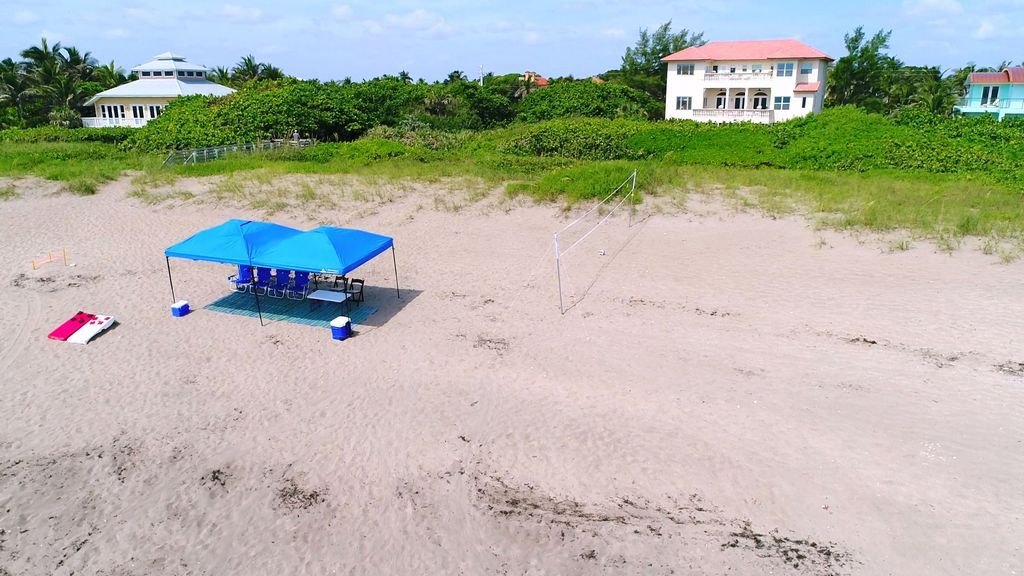 Blue canopy on beach with beach house in the background.